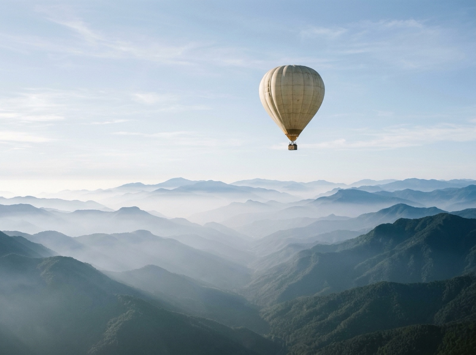 Pale hot air balloon above a valley in morning haze